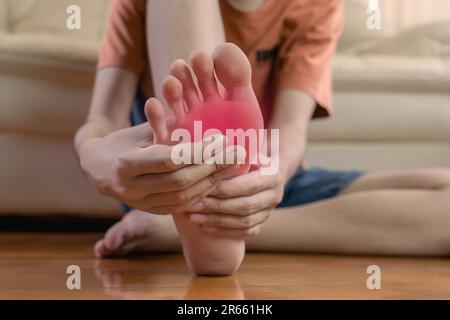 Der junge Mann hält die Hände am Fuß und leidet unter Schmerzen im Fuß. Teenager nutzen die Handmassage, um Muskeln zu entspannen und auf dem Sofa zu sitzen. Gesundheitsfürsorge und Podiatrie Stockfoto