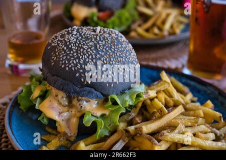 Nahaufnahme eines köstlichen schwarzen Burgers mit pommes frites in einem Restaurant in Bonifacio Stockfoto