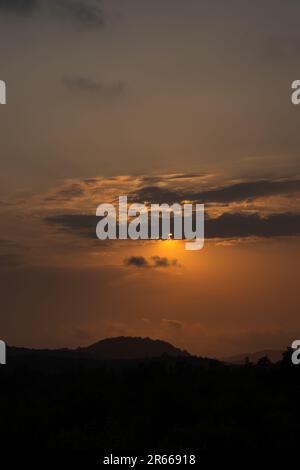 Die Sonne geht unter und malt den Himmel in einem dramatischen orangefarbenen Farbton. Silhouette Wolken sitzen an diesem ruhigen Nachglühen und schaffen ein atemberaubend schönes l Stockfoto