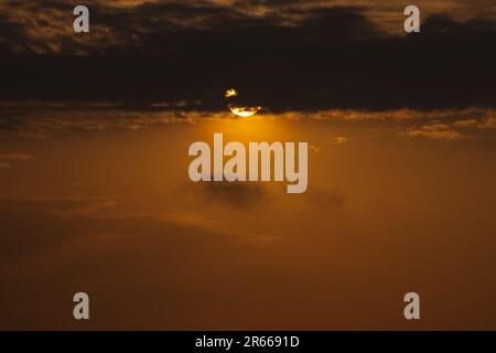 Atemberaubende Pink- und Orangentöne säumen den Morgenhimmel mit einer brennenden Sonne, die über dem fernen Horizont ihren Höhepunkt erreicht. Ein sanftes Nachglühen strahlt aus BE Stockfoto