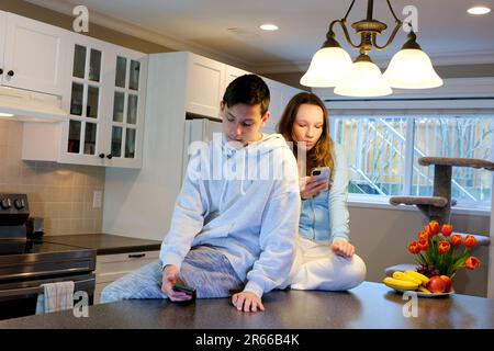 Teenager verbringen Zeit mit Telefonen Junge und ein 13-16-jähriges Mädchen sitzen in der Küche auf dem Tisch jeder ist beschäftigt mit seinem Gadget erstes Date, keine Zeit, um im Internet auf sozialen Netzwerken zu sitzen, um Zeit zu verlieren Stockfoto