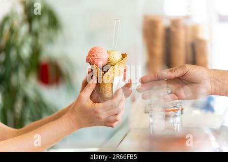 Ein Mann serviert einer Frau ein Eis mit verschiedenen Geschmacksrichtungen Stockfoto