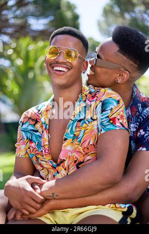 Glückliches junges schwules Paar mit Sonnenbrille, das sich umarmt und lacht Stockfoto