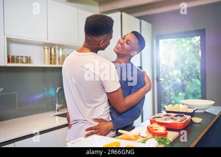 Glückliches, liebevolles, junges schwules Paar, das zu Hause umarmt und kocht Stockfoto
