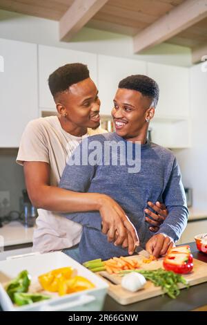 Fröhliches, liebevolles junges schwules Paar, das zu Hause kocht und umarmt Stockfoto