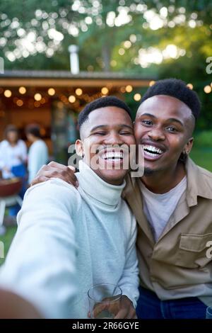 Selfie-POV-Porträt glückliches junges schwules männliches Paar, das im Garten lacht Stockfoto