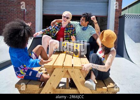 Fröhliche junge Freunde hören Musik mit der Boom Box am Picknicktisch Stockfoto