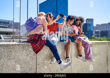 Junge Freunde, die in der sonnigen Stadt Smartphones benutzen Stockfoto