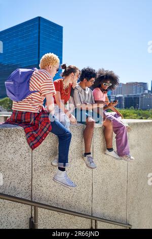 Junge Freunde, die in der sonnigen Stadt auf dem Vorsprung rumhängen Stockfoto