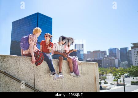 Junge Freunde, die in der sonnigen Stadt auf dem Vorsprung rumhängen Stockfoto