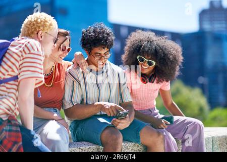 Junge Freunde, die Smartphones in der sonnigen Stadt benutzen Stockfoto