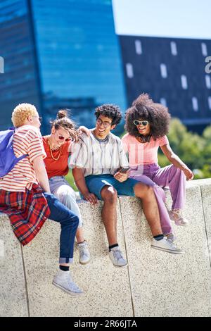 Junge Freunde, die lachen, auf dem Vorsprung in der sonnigen Stadt rumhängen Stockfoto