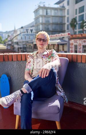 Selbstbewusster, cooler junger Mann, der auf einem sonnigen Stadtdach sitzt Stockfoto