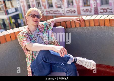 Portrait glücklicher junger Albino-Mann, der auf einem sonnigen Stadtdach sitzt Stockfoto