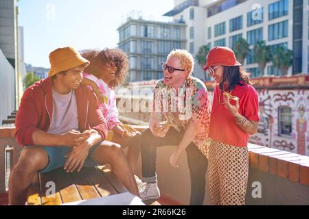 Fröhliche junge Freunde hängen rum und essen Pizza auf dem sonnigen Dach Stockfoto