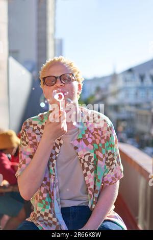 Ein junger Mann bläst Blasen auf dem sonnigen Balkon Stockfoto