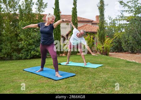 Glückliches, aktives Seniorenpaar, das Yoga im Villengarten praktiziert Stockfoto