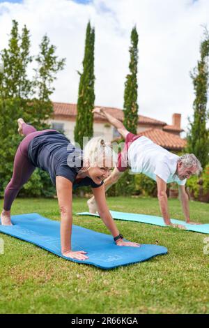 Lächelndes, aktives Seniorenpaar, das Yoga im Villengarten praktiziert Stockfoto