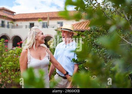 Glückliches Seniorenpaar, das im Garten vor der Sommervilla spaziert Stockfoto