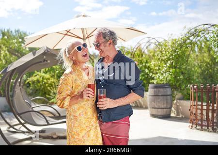 Glückliches Seniorenpaar, das lacht und Cocktails auf der Sommerterrasse trinkt Stockfoto