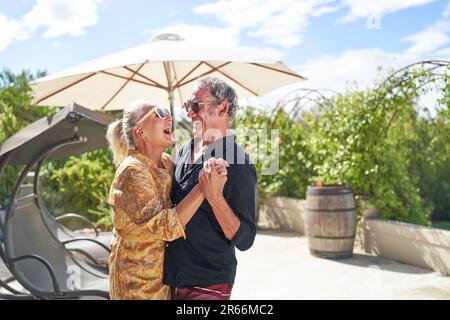 Glückliches, sorgenfreies Seniorenpaar, das auf der Sommerterrasse lacht und tanzt Stockfoto