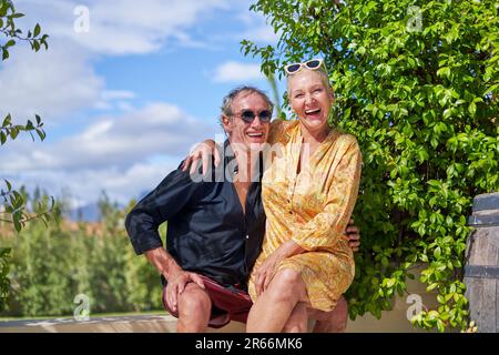 Portrait glückliches, sorgenfreies Seniorenpaar, das auf der sonnigen Sommerterrasse lacht Stockfoto