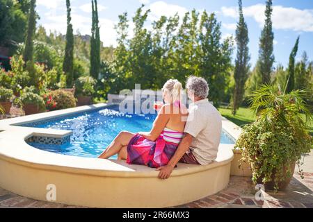 Seniorenpaar, das sich im sonnigen Sommerschwimmbad erholt Stockfoto