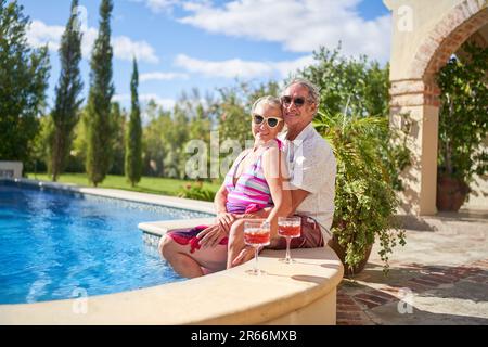 Portrait glückliches Seniorenpaar, das sich im sonnigen Sommerschwimmbad entspannt Stockfoto