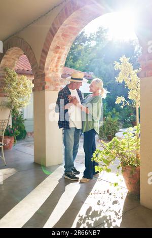 Glückliches, liebevolles Seniorenpaar, das auf der sonnigen Villa-Terrasse tanzt Stockfoto