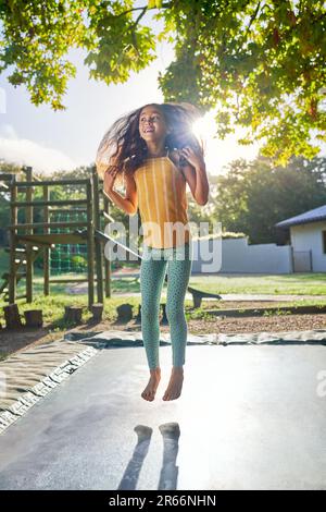 Ein sorgloses, barfuß-Mädchen, das auf Trampolin in einem sonnigen Garten springt Stockfoto