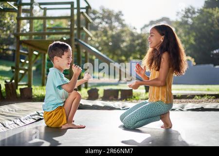 Fröhliche Geschwister, die auf dem sonnigen Trampolin klatschen Stockfoto