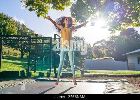 Ein sorgenfreies Mädchen, das auf Trampolin in einem sonnigen Garten springt Stockfoto