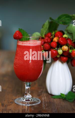 Erdbeercocktail in einem Nebelglas und eine weiße Keramikvase mit Erdbeerzweigen und reifen roten Beeren Stockfoto