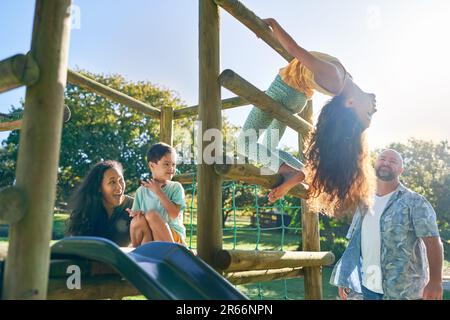 Fröhliche Familie, die auf Spielplatzgeräten im sonnigen Garten spielt Stockfoto