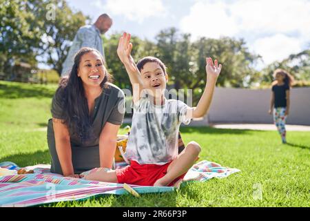 Glückliche Mutter, die den süßen Sohn mit Down-Syndrom beim Essen im Park beobachtet Stockfoto