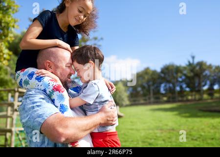 Vater hält, trägt Tochter und Sohn mit Down-Syndrom im Park Stockfoto