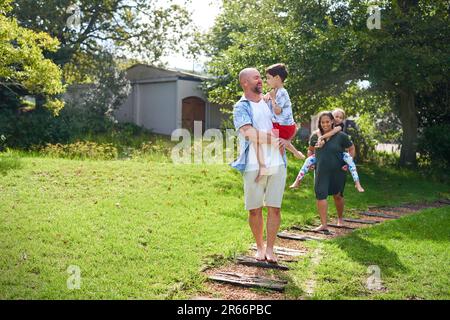 Glückliche Eltern, die Tochter und Sohn auf dem Weg in den sonnigen Garten tragen Stockfoto