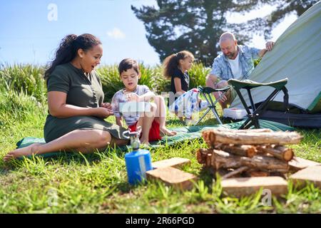 Familienkochen und Pitching-Zelt auf dem sonnigen Sommercampingplatz Stockfoto