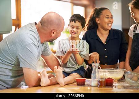 Glücklicher Junge mit Down-Syndrom, der mit der Familie zu Hause in der Küche backt Stockfoto