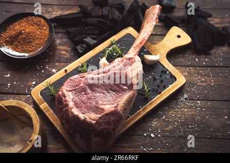 Getrocknetes gereiftes rohes Tomahawk Black angus Prime Rindfleisch-Kotelett mit Salz, Pfeffer, Rosmarin, Knoblauch, Holzkohle und einem Messer Stockfoto