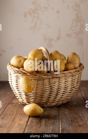 Korb aus Korb mit Kartoffeln auf einem braunen Holztisch mit beigefarbenem Hintergrund Stockfoto