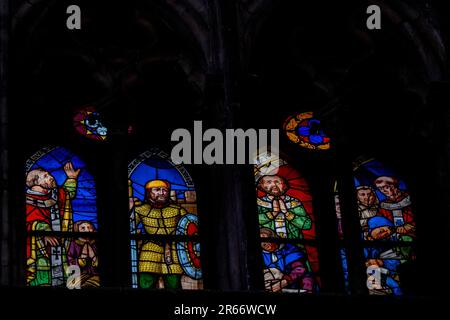 Mehrfarbige mittelalterliche Buntglaspaneele, die Geistliche, Soldaten und Heilige in einer steinernen gotischen Tracery in einer Kathedrale darstellen. Beleuchtete Fenster Stockfoto