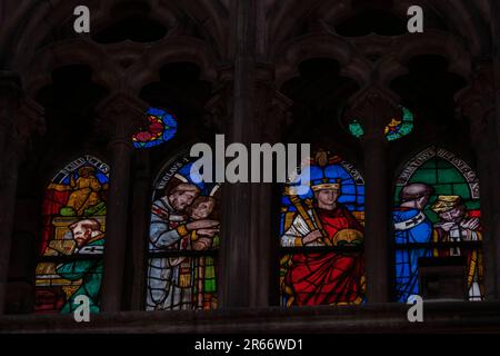 Mehrfarbige mittelalterliche Buntglaspaneele, die Klerus, Monarchen und Heilige in einer Steingothik in einer Kathedrale darstellen. Beleuchtete Fenster Stockfoto