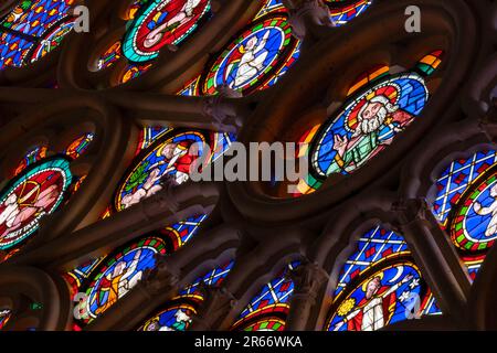 Buntglaspaneele aus der mittelalterlichen Ära mit Rosenfenstern, die Heilige und Engel in einer steinernen gotischen Tracery in einer Kathedrale zeigen Stockfoto