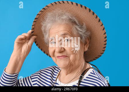 Seniorin mit Sonnencreme im Gesicht vor blauem Hintergrund, Nahaufnahme Stockfoto