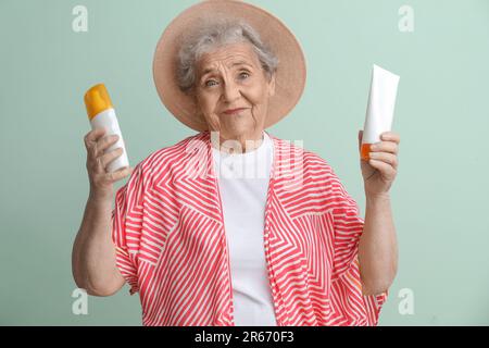 Seniorin mit Sonnencreme auf grünem Hintergrund Stockfoto
