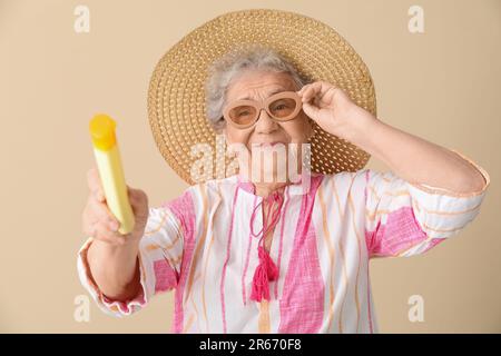 Seniorin mit Sonnencreme auf beigem Hintergrund Stockfoto