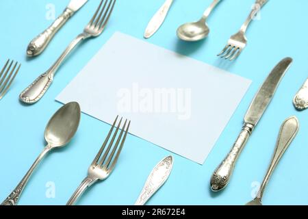 Rahmen aus unbeschrifteter Karte und Besteck aus Edelstahl auf blauem Hintergrund Stockfoto