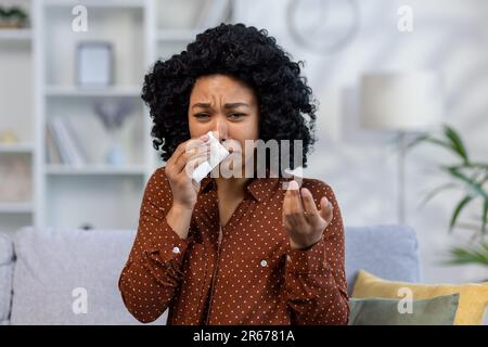 Junge afroamerikanische Frau, die weint, Schmerzen hat, Probleme hat, mit der Kamera telefoniert, psychologische Hilfe und Unterstützung benötigt. Wischte die Tränen mit einer Serviette ab. Stockfoto