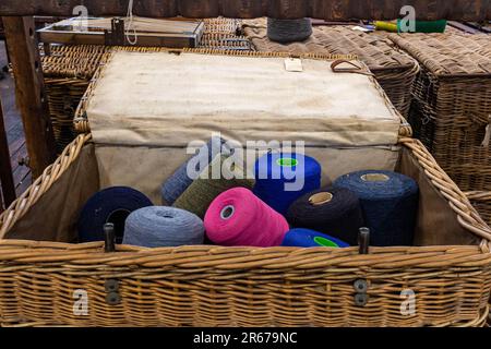 Auf einem Holztisch sind verschiedene bunte Garne in einem gewebten Korb zu sehen Stockfoto